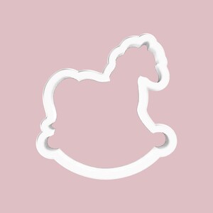 May include: A white, outline-style cookie cutter in the shape of a rocking horse. The cutter is set against a soft, pink background. The design features the horse's head, body, and curved rockers, perfect for baking themed treats.