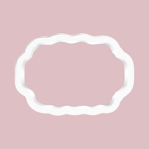 May include: A white, scalloped-edge cookie cutter in a rectangular shape. The cutter is made of a solid white material and is set against a soft pink background. The design is simple and clean, suitable for baking.