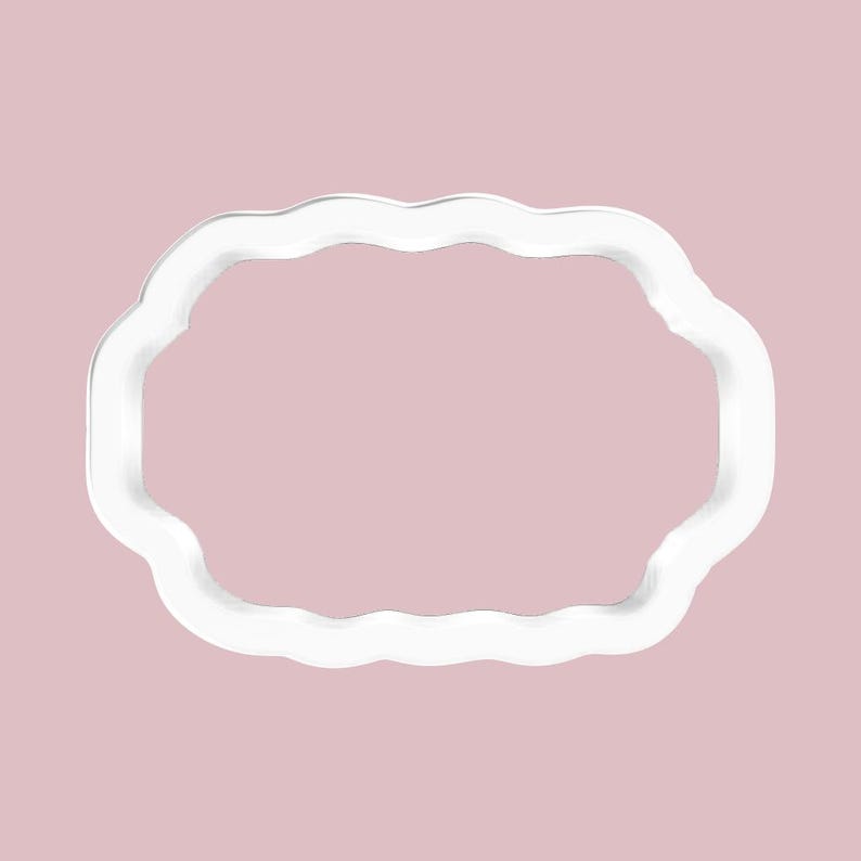 May include: A white, scalloped-edge cookie cutter in a rectangular shape. The cutter is made of a solid white material and is set against a soft pink background. The design is simple and clean, suitable for baking.