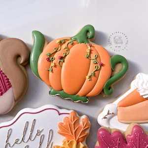 May include: An orange pumpkin-shaped cookie with green accents and floral vines. The cookie is decorated with intricate details and is part of a collection of fall-themed cookies. Other cookies include a squirrel, a leaf, and a slice of pie.