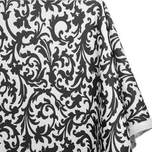 May include: A white fabric with a repeating black floral pattern. The design features stylized leaves and swirling lines, creating a classic damask style. The fabric is folded, showing the edge of the material.