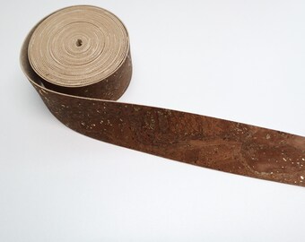 May include: A roll of brown cork ribbon with gold flecks. The ribbon is rolled up and the end is unfurled, showing the texture of the cork.