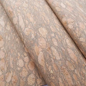 May include: Close-up of a sheet of cork fabric with a light brown and beige mottled pattern. The cork has a natural, organic texture.