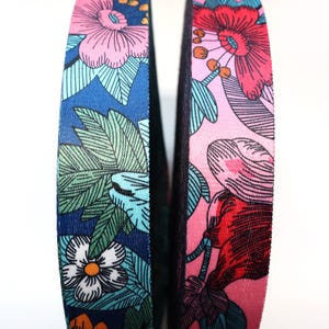 May include: Two floral patterned ribbons. One ribbon features a navy blue background with white flowers, green leaves, and orange accents. The other ribbon has a pink background with red and pink flowers and blue accents.