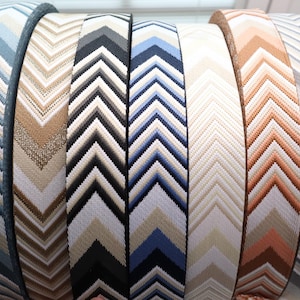 May include: A collection of woven straps with a chevron pattern in various colors. The straps include shades of blue, beige, brown, black, and white. The straps are likely used for bags or other accessories.