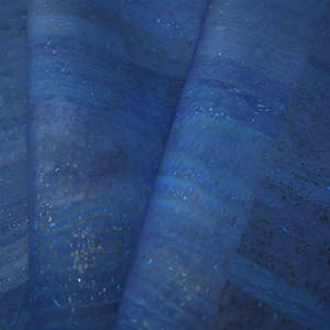 May include: A close-up of a blue cork fabric with a textured, slightly grainy surface. The fabric has a subtle sheen and a slightly iridescent quality.