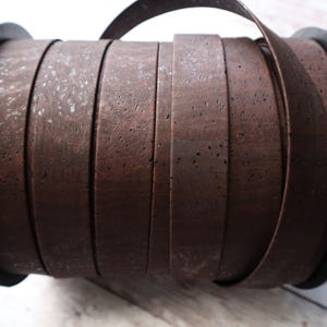 May include: A roll of brown cork ribbon, wound around a black spool. The ribbon is textured and has a natural, rustic look.