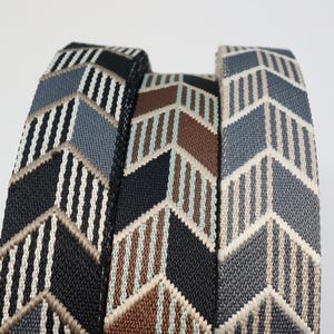 May include: Three rolls of woven fabric webbing featuring a repeating chevron pattern. The left roll displays black, white, and grey stripes. The center roll shows black, brown, and light blue stripes. The right roll features grey and beige stripes.
