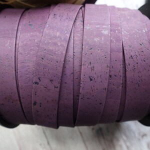 May include: A roll of purple cork ribbon with a speckled texture. The ribbon is wound around a black spool.
