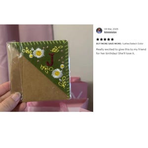 May include: A handmade bookmark with a green embroidered corner featuring white daisies and a red letter "J". The bookmark is packaged in clear plastic. The text on the image says "BUY MORE SAVE MORE: 1 Letter/Select Color".
