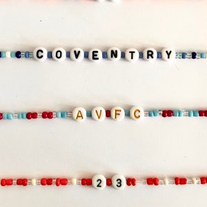Puede incluir: Una colecci&oacute;n de pulseras de cuentas con cuentas blancas con letras y n&uacute;meros. Las pulseras muestran las palabras "SMITH", "COVENTRY" y "AVFC", junto con los n&uacute;meros "91" y "23". Las cuentas son de varios colores, incluyendo rojo, naranja y azul.