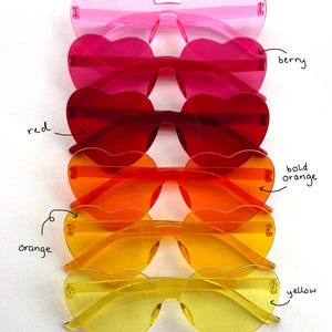 May include: A collection of heart-shaped sunglasses in various colors, including pink, berry, red, bold orange, orange, and yellow. The sunglasses are arranged in a vertical stack, showcasing their vibrant hues and unique design.