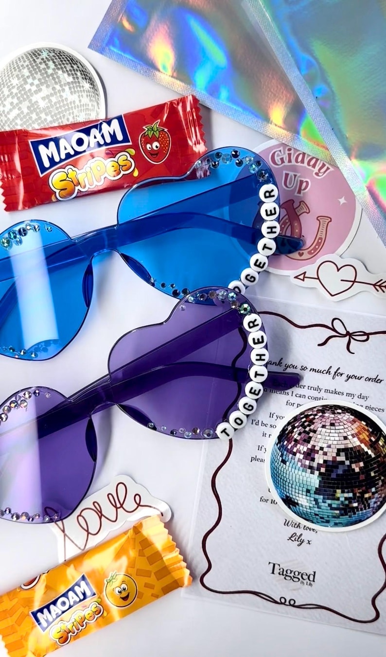 May include: Heart-shaped sunglasses in blue and purple with rhinestone accents. The sunglasses have the word "TOGETHER" spelled out on the frames. The image also includes candy, stickers, and a disco ball.