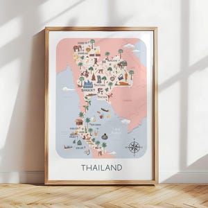Op de afbeelding: Een ingelijste kaart van Thailand in roze en blauw, met illustraties van bezienswaardigheden en locaties. Het woord "THAILAND" staat onderaan afgedrukt. De lijst is licht van kleur, de achtergrond is wit.