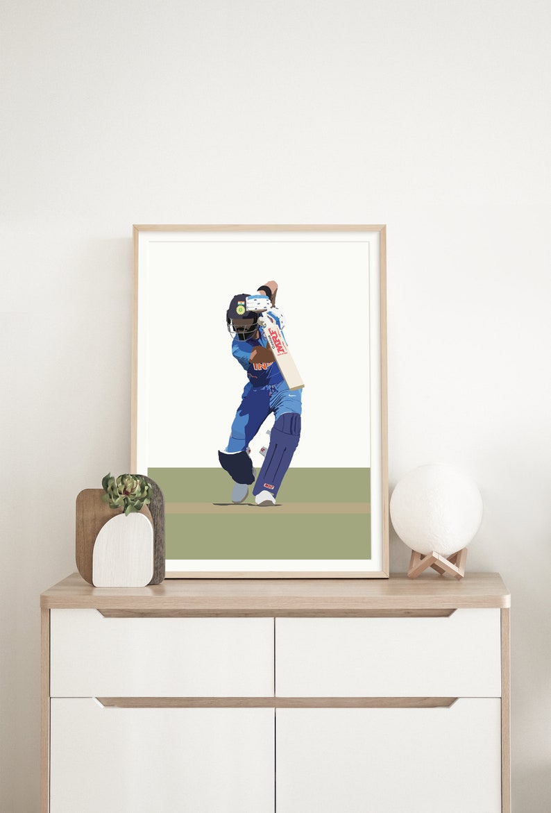 May include: A framed illustration of a cricket player in a blue uniform swinging a bat. The player is wearing a helmet and is in a batting stance. The background is a green field.