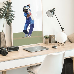 May include: A framed illustration of a cricket player in a blue uniform swinging a bat. The player is wearing a helmet and is in a batting stance. The background is a green field.