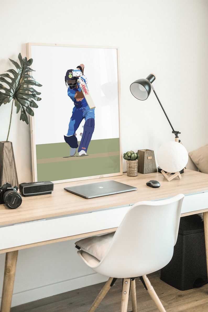 May include: A framed illustration of a cricket player in a blue uniform swinging a bat. The player is wearing a helmet and is in a batting stance. The background is a green field.