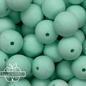 May include: A close-up of a pile of light green silicone beads. The beads are round and have a hole in the center. They are perfect for making jewelry or other crafts.