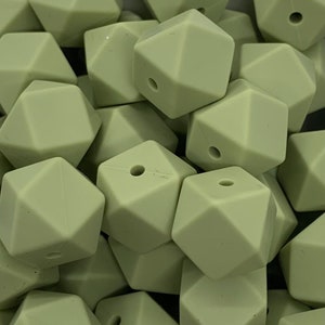 May include: A close-up of a pile of sage green silicone teething beads. The beads are shaped like a geometric diamond with a hole in the center.