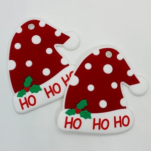 May include: Two red and white Christmas ornaments shaped like Santa hats with white polka dots and the words "Ho Ho Ho" on the bottom.