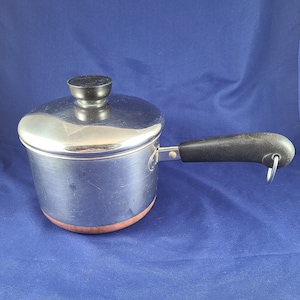May include: A silver saucepan with a copper bottom and a black handle. The saucepan has a lid with a black knob.