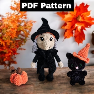 May include: A crocheted witch doll wearing a black hat and dress, a black crocheted cat doll wearing an orange hat, and a crocheted orange pumpkin. The dolls and pumpkin are on a wooden surface with autumn leaves in the background.