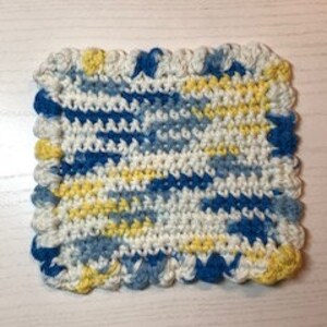 May include: A crocheted dishcloth in white, blue, and yellow with a scalloped edge.