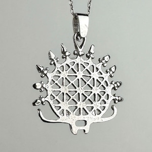 May include: A silver-colored pendant necklace featuring a hedgehog design. The pendant has a geometric pattern within the body and a spiky outline. The necklace chain is also silver and hangs against a light gray background.