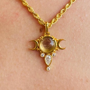 Puede incluir: Un collar de cadena de oro con un colgante que presenta tres lunas crecientes y una gema redonda y transparente en el centro. El colgante está acentuado con gemas transparentes más pequeñas.