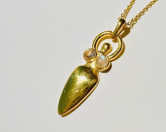 May include: A gold necklace featuring a pendant shaped like a woman with two moonstone accents. The pendant hangs from a delicate gold chain.