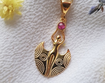 May include: Gold pendant necklace featuring a stylized female figure with outstretched arms holding a pink gemstone. The figure is set against a crescent moon design with concentric circles.