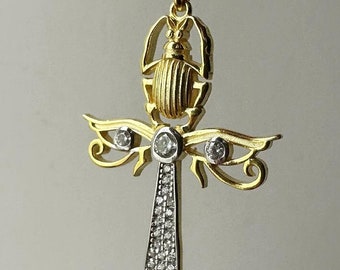 Op de afbeelding: Gouden ketting met hanger in de vorm van een gedetailleerd Ankh-kruis met een scarabée-ontwerp. De hanger is versierd met heldere zirkonia-stenen.