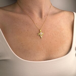 May include: Gold-toned necklace featuring a pendant with a central, round, light-colored stone, flanked by crescent moon shapes. The pendant also includes smaller, clear, teardrop-shaped and round accents. The necklace is worn against a white top.