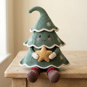 May include: A knitted plush toy shaped like a green Christmas tree with a curved top, a smiling face, and pink cheeks. The tree features white snowflake embroidery, a cream-colored trim, and holds a yellow star. It has brown feet with red cuffs.