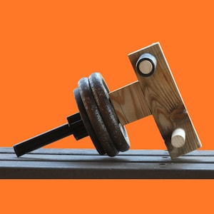 May include: A wooden weightlifting device with a black metal bar and weight plates. The device is made of wood and has a simple design.