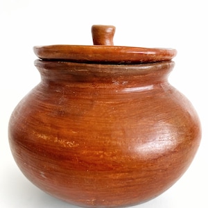 May include: A handcrafted, brown ceramic pot with a lid. The pot has a rounded body and a slightly textured surface. The lid has a small handle on top. The pot is likely used for storage or decoration.