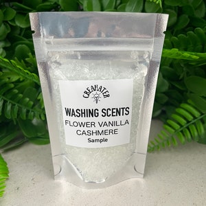 May include: A small clear plastic bag filled with white laundry scent beads. The bag has a white label with the text "CREAHATER WASHING SCENTS FLOWER VANILLA CASHMERE Sample".