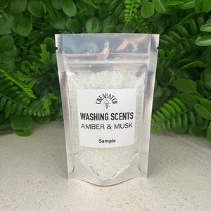 May include: A small silver pouch with a white label that reads "Washing Scents Amber & Musk Sample". The pouch contains clear crystals.