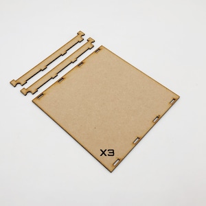 May include: A set of three unfinished wooden pieces for building a small box. The pieces are made of brown cardboard and have a simple design. The text "X3" is printed on one of the pieces.