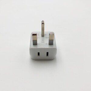 May include: White three-prong UK plug adapter with a silver colored metal prongs. The adapter has the letters L, N, and E printed on it.