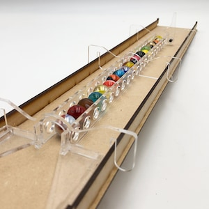 Op de afbeelding: Een houten knikkerbaan spel met een transparante acrylbaan en gekleurde knikkers. De baan is gemaakt van meerdere secties die aan elkaar zijn verbonden. De knikkers rollen de baan af.