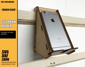 May include: A laser-cut wooden phone holder designed for a French cleat system. The holder is made for a 3mm material and is compatible with a standard-sized smartphone. The holder is labeled with the text "iPhone" and has a cutout for the phone's camera. The holder is laser-ready and comes in SVG, DXF, and LBRN file formats.