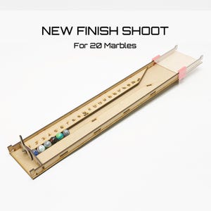 Puede incluir: Un juego de canicas de madera con una pista numerada para 20 canicas. La pista está hecha de madera y tiene un acabado claro. Las canicas son visibles en la pista. La pista está etiquetada "NEW FINISH SHOOT" y "For 20 Marbles".
