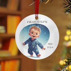 May include: A white round Christmas bauble featuring a blue and white illustration of a baby taking their first steps. The bauble is inscribed with the text "FIRST STEPS" and "TED 2024".