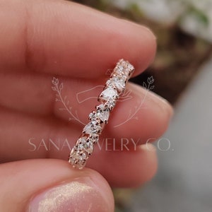 May include: A delicate rose gold band with a row of sparkling round diamonds. The band is shown on a finger.
