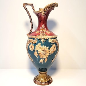 May include: A large, ornate ceramic pitcher with a green and red body, gold accents, and a bamboo-style handle. The pitcher features a floral design with raised details.