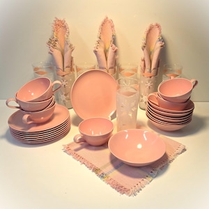 May include: A set of pink vintage teacups, saucers, and plates with a matching pink bowl. The set also includes four clear glasses with a snowflake design and four pink napkins with fringe.