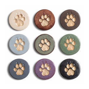 May include: Nine ceramic coasters featuring a paw print design in a variety of colours, including beige, brown, grey, blue, green, purple, and black.