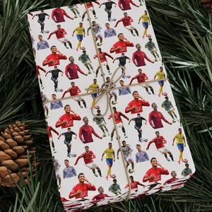 May include: White wrapping paper with a repeating pattern of soccer players in red and white uniforms. The players are in various poses, some are kicking the ball, some are running, and some are celebrating.