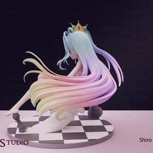 Pu&ograve; includere: Statuetta di un personaggio seduto con lunghi capelli dai colori pastello, con una corona d'oro. La figura poggia su una base a scacchi con pezzi degli scacchi. Visibile il logo Pink Studio. I capelli sono multicolore.